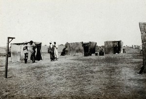 view Fayum, Egypt: a plague hospital on the First World War Western Front: a group of basic huts with soldiers and egyptian men standing to one side. Photograph, 1914/1918.