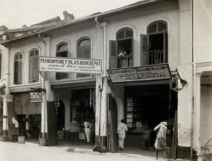 view Kuala Lumpur, Malaysia: an arcade of shops with a road sweeper at work in the street. Photograph, 1915/1925.