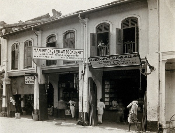 Kuala Lumpur, Malaysia: an arcade of shops with a road sweeper at work in the street. Photograph, 1915/1925.