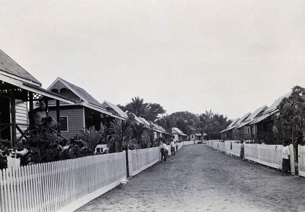 Stoner Village, Chiengmai Leper Asylum, Thailand: patients in a street lined with wooden houses. Photograph, 1921.