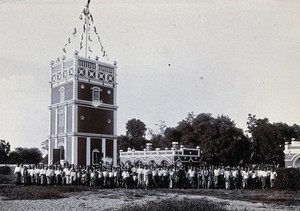 view Chiengmai Leper Asylum, Thailand: patients grouped at the foot of the large water tower. Photograph, 1921.