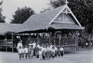 view Chiengmai Leper Asylum, Thailand: children outside the grass-roofed temporary school for uninfected children of leprosy patients. Photograph, 1921.