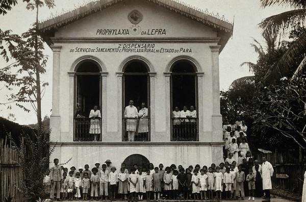 The Therapeutic Institute for Leprosy, Tocunduba, Pará, Brazil: patients and staff are grouped outside and at the balconies to large, arched windows of a hospital building. Photograph, 1890/1910.