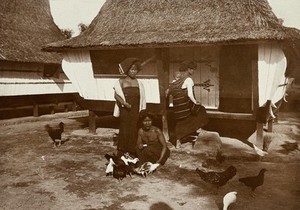 view Three women (one carries a baby on her back in a fabric sling) with poultry, outside a wooden, thatched-roof house (of a leprosy asylum ?). Photograph, 1890/1910.