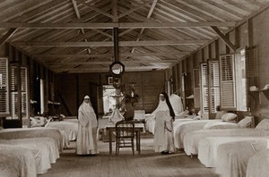 view Leper asylum, Port of Spain, Trinidad: two nuns (working as nurses) in a hospital ward with empty beds. Photograph, 1890/1910.