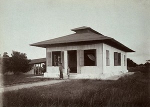 view St. John's Island, Singapore: the small-pox camp; two children stand on the steps and two men at the window of a white house with large shuttered windows. Photograph by A. R. Wellington, 1909.