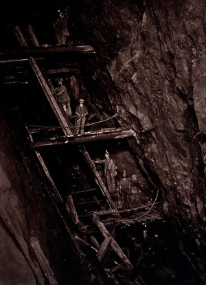 view Dolcoath tin mine, Camborne, Cornwall: miners in a mine shaft, standing on wooden platforms connected by ladders. Photograph by J. C. Burrow, 1890/1910.