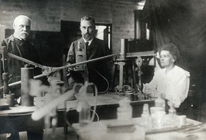 view Marie and Pierre Curie (centre) with a man, using equipment in their laboratory, Paris. Photograph, ca. 1900.