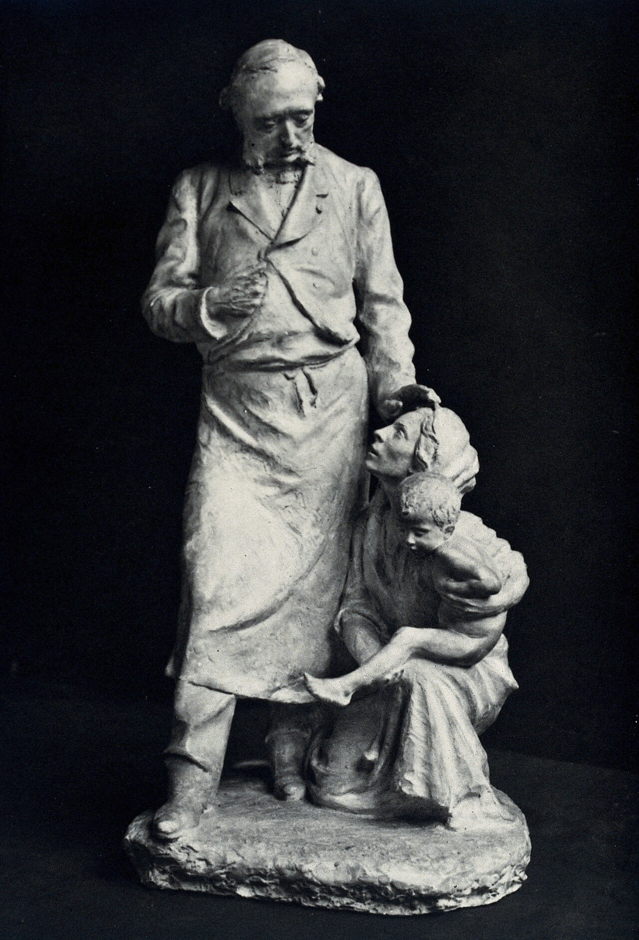 Léopold Ollier, an orthopaedic surgeon, comforting a woman holding a child kneeling at his feet. Photograph of a sculpture by E. Destot., 1900-1920, by Étienne Destot