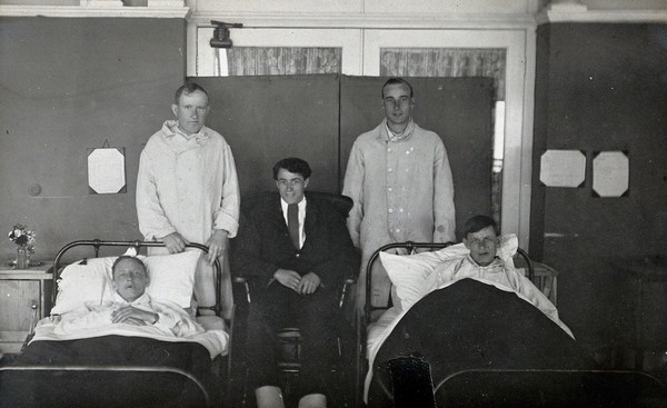 First World War wounded soldiers: group portrait: two lying in hospital beds; two standing; one seated. Photograph, 1914/1918.