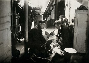 view World War One: a Royal Naval hospital ship: bandaging a wounded man on a stretcher. Photograph, 1914/1918.