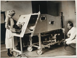 view An iron lung, St. Bartholomew's Hospital, London: a patient inside a Drinker respirator, attended to by a nurse and a doctor. Photograph, ca. 1930( ?).