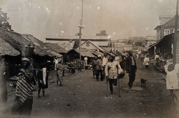 Freetown, Sierra Leone: local people, including an amputee on crutches, are shown walking along one of the principal streets. Photograph, 1910/1920.