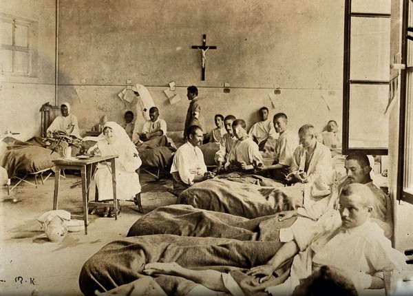 Italian Red Cross Hospital ward, during World War I: bedridden male patients are shown reading, playing cards etc, watched over by a female nurse seated at a small table. Photograph, 1914/1918.