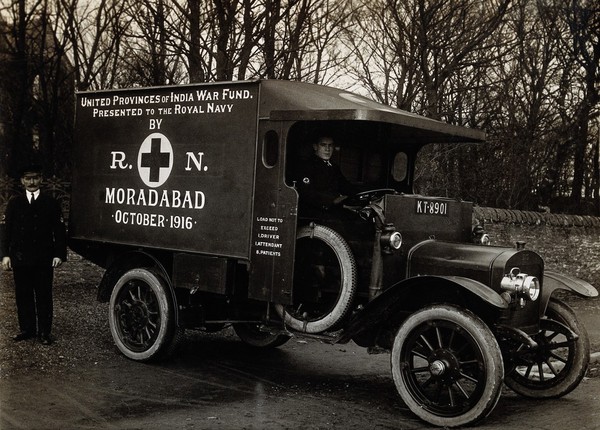 Ambulance presented to the British Royal Navy by the city of Moradabad, India in 1916: a uniformed ambulanceman is shown at the wheel, while another stands at the rear of the vehicle. Photograph, 1916/1918.
