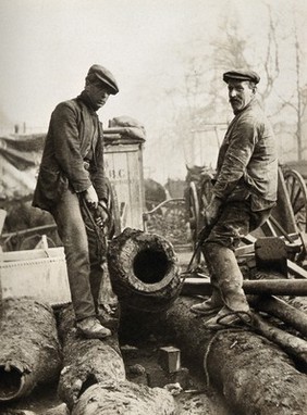 Two workmen unearthing large wooden pipes dating from 1676, excavated at Marylebone Road, London. Photograph, 1937.