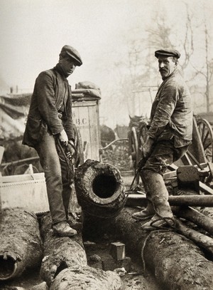 view Two workmen unearthing large wooden pipes dating from 1676, excavated at Marylebone Road, London. Photograph, 1937.