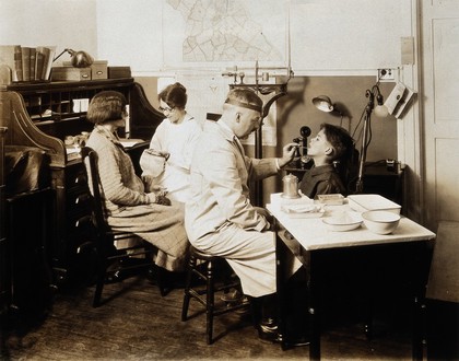 A Pennsylvania State tuberculosis clinic: a male doctor is shown examining the tongue of a boy, while a female medical practitioner takes the pulse of a woman. Photograph, 1925/1935?.