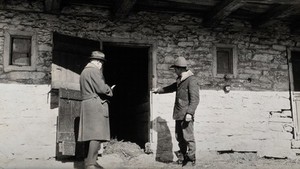 view A health officer inspecting dairy stables, Pennsylvania: a dairy worker points to the open door of a stable, while the health officer takes notes. Photograph, 1920/1935?.