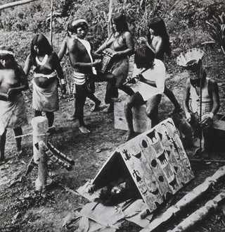 Panama: a Choco Indian medicine man with musicians during a ceremony to heal a sick boy lying beneath a shelter bearing symbols. Photograph of a process print, ca. 1920 (?).