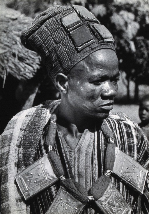 Africa: a man wearing a hat and large metal and yarn necklace. Photograph (by Kurt Lubinski ?), 1940/1960.