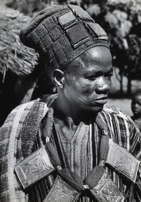 Africa: a man wearing a hat and large metal and yarn necklace. Photograph (by Kurt Lubinski?), 1940/1960.