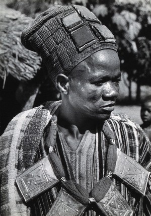 view Africa: a man wearing a hat and large metal and yarn necklace. Photograph (by Kurt Lubinski?), 1940/1960.