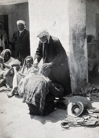 Sudan: a barber shaving the head of a man seated in the street. Photograph, ca. 1920.