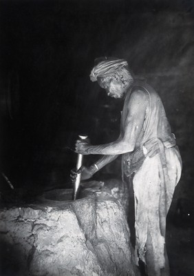 Sudan: a man grinding with a large pestle and mortar. Photograph, ca. 1920.