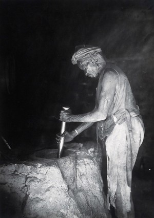 view Sudan: a man grinding with a large pestle and mortar. Photograph, ca. 1920.