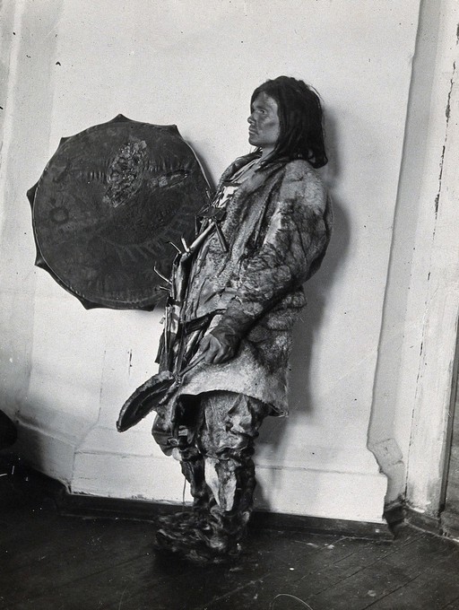 Siberia: an Ostiak medicine man wearing animal skins and with a shield: studio portrait: side view. Photograph, ca. 1920 (?) of a photograph by Marya Czaplicka, 1914/1915.