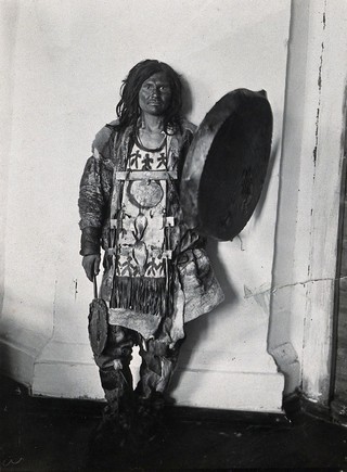 Siberia: an Ostiak medicine man wearing animal skins, holding a shield: studio portrait: front view. Photograph, ca. 1920 (?) of a photograph by Marya Czaplicka, 1914/1915.