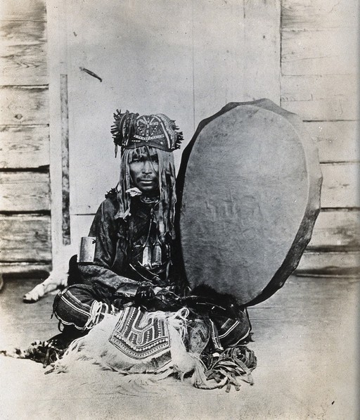 Siberia: a Tungus medicine man in ceremonial dress, seated holding a drum. Photograph, ca. 1920 (?) of a photograph by Marya Czaplicka, 1914/1915.