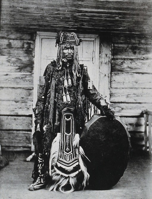 Siberia: a Tungus medicine man in ceremonial dress, standing holding a drum. Photograph, ca. 1920 (?) of a photograph by Marya Czaplicka, 1914/1915.