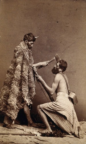 view Two Maori men, simulating armed attack with a hatchet and a spear(?). Photograph, 18--.