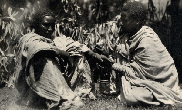 Ethiopia: a Gurage woman tattooing another on the wrist. Photograph by H.V. Meyerowitz, 19--.