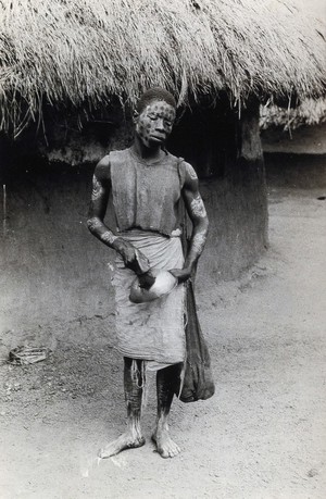 view Sierra Leone: a tattooed man of the Kissi people collecting money. Photograph, 19--.