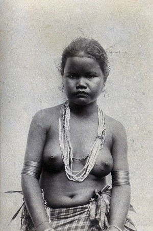 view A young woman wearing a necklace of beads and a checked skirt. Photograph.