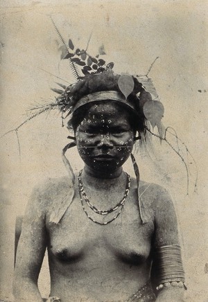 view A young woman with extensive scarification on her face, wearing a hat of foliage: front view. Photograph.