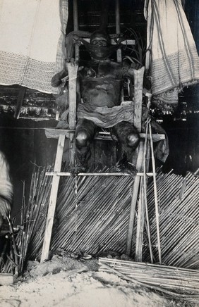 Philippines: the body of a wealthy dead man displayed seated on a high chair after having been smoked for 15 days. Photograph, 19--.