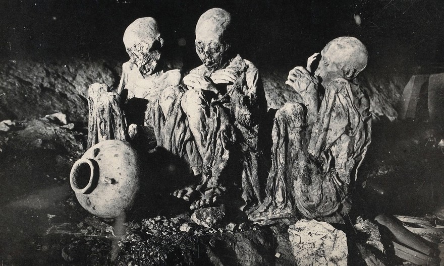 Philippines: the dead and smoked bodies of three people seated on the ground. Photograph, 19--.