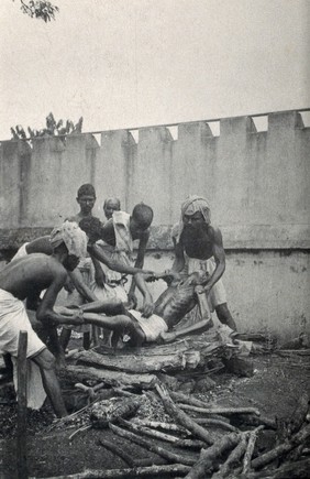 Calcutta, West Bengal: young men placing the dead body of a man on a funeral pyre. Photograph.