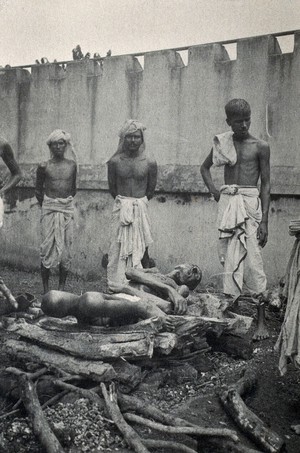 view Calcutta, West Bengal: young men standing by a funeral pyre on which they have placed the dead body of a man. Photograph.
