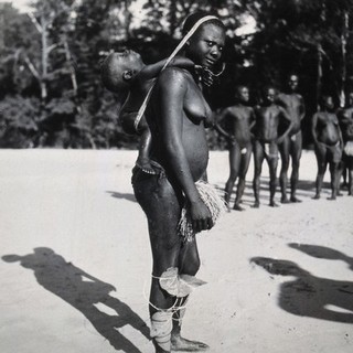 Africa: a woman carrying her baby on her back, supported by a strap around her head. Photograph, 1930/1960.