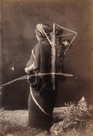 view An Araucanian woman in Chile carrying a sleeping child on her back in a wooden carrier, supported by a strap around her head. Photograph, ca. 1913.
