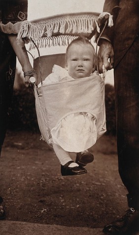 A baby in a carrier made from canvas sailor's trousers in Southend-on-Sea, England. Photograph by Cyril Norwood, 1922.