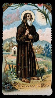 Saint Francis of Paula holding his walking stick with both hands and looking at the sun; church and mountains in the background. Colour lithograph, ca. 1898.