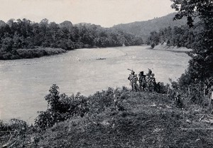 view Sarawak: three men standing by the Baram River. Photograph.