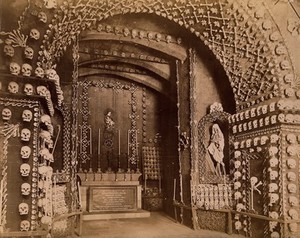 view An altar bearing a Latin inscription surrounded by an array of human skulls and bones and a cloaked skeleton. Photograph by J. Taylor, c. 1881.