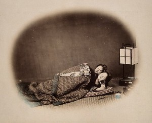 view Two Japanese women asleep under a quilt. Coloured photograph by Felice Beato, ca. 1870.